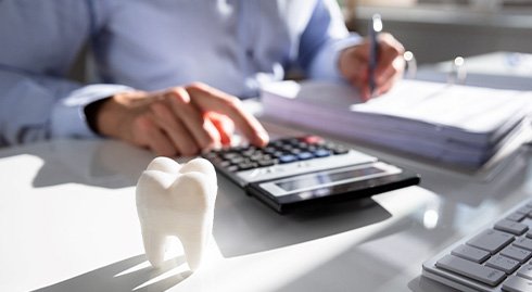 Someone working with invoices and calculator at white desk with large model tooth