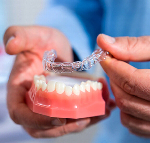Dentist placing clear aligner on mold of teeth
