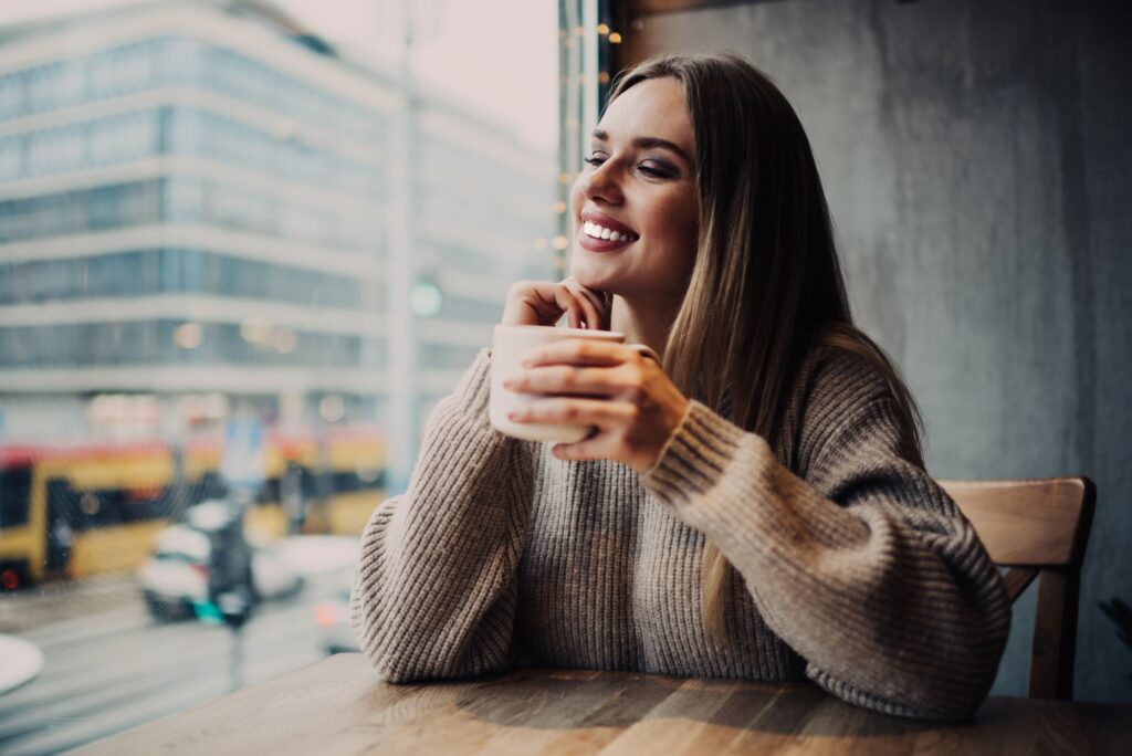 Woman in brown sweater at cafe smiling with veneers